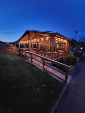 Un bâtiment en bois doté d’un patio couvert, d’un espace extérieur aménagé avec des sièges et d’une clôture en bois.