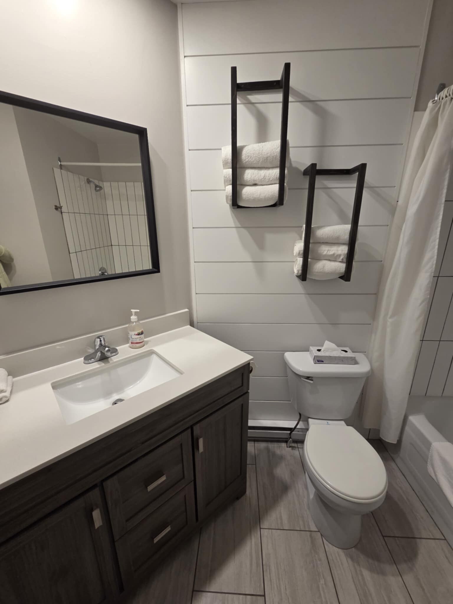A modern bathroom with a white sink, dark wooden vanity, a toilet, and a shower curtain.