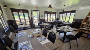 A dining area with multiple tables and chairs, large windows, and a view of the outdoors.
