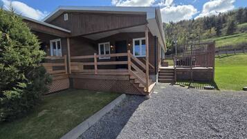 Eine Holzhütte mit Veranda, einem Schotterweg und einem bewaldeten Hang im Hintergrund.