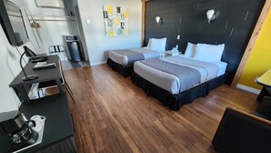 A modern hotel room with two beds, a desk, a coffee machine, and a flat-screen TV.