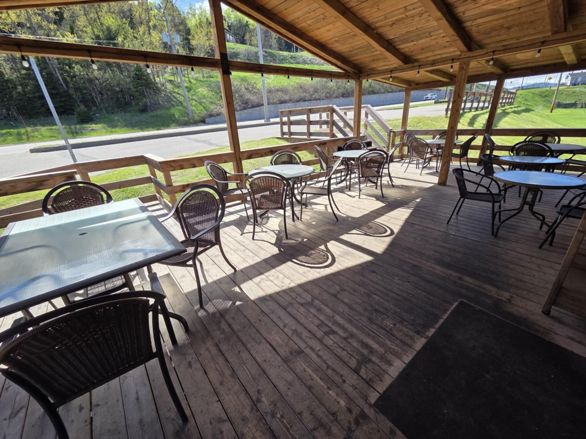 Une terrasse extérieure avec des tables et des chaises en bois, ainsi qu’un espace couvert offrant une vue sur le paysage environnant.
