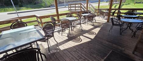 Une terrasse extérieure avec des tables et des chaises en bois, ainsi qu’un espace couvert offrant une vue sur le paysage environnant.
