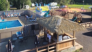 A pool area with lounge chairs, a thatched-roof structure, and a playground.