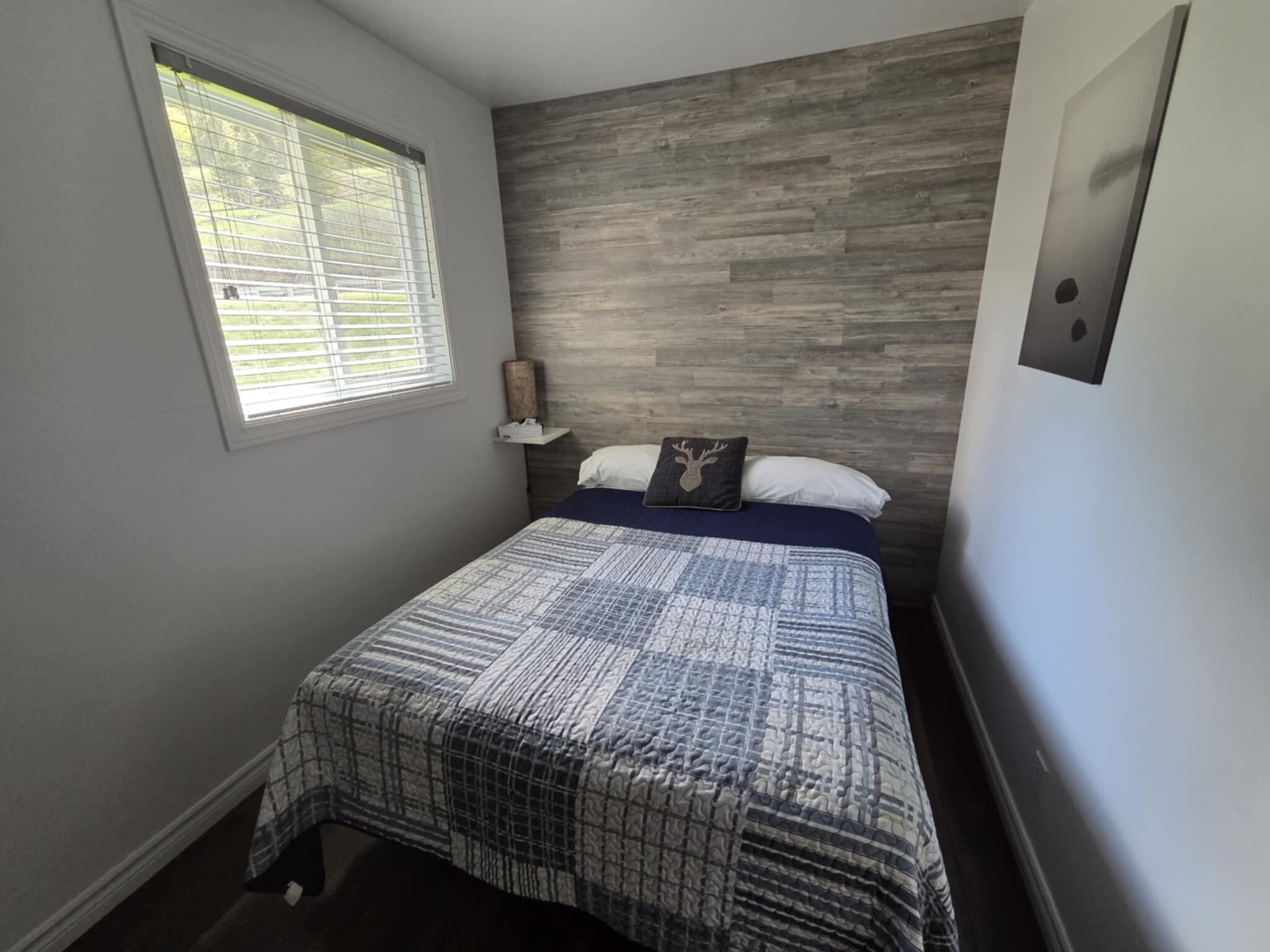 A bedroom with a bed, a window, a wooden headboard, and a wall-mounted light fixture.