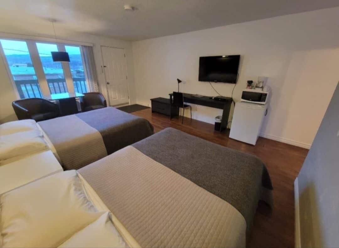 A hotel room with two beds, a desk, a TV, and a balcony with a view.
