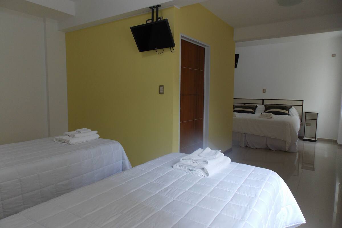 Una habitación de hotel con dos camas, un televisor montado en la pared y una puerta de madera.