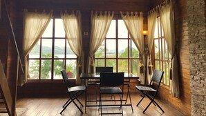 A room with a wooden floor, a table, and two chairs. There are large windows with curtains, and a view of greenery and hills outside. - Sauce Lodge Laguna Azul (Sauce)