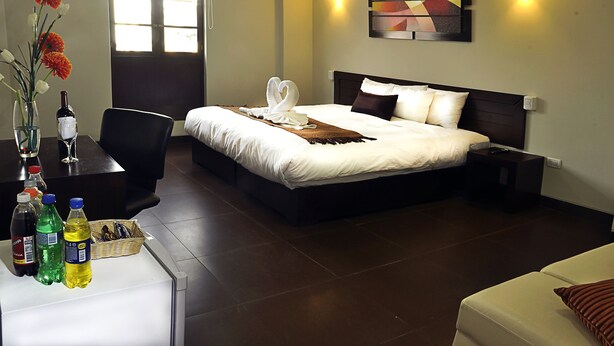 A hotel room with a large bed, a desk with a vase of flowers, and a window. - Hoteles Riviera - Mansión (Arequipa)