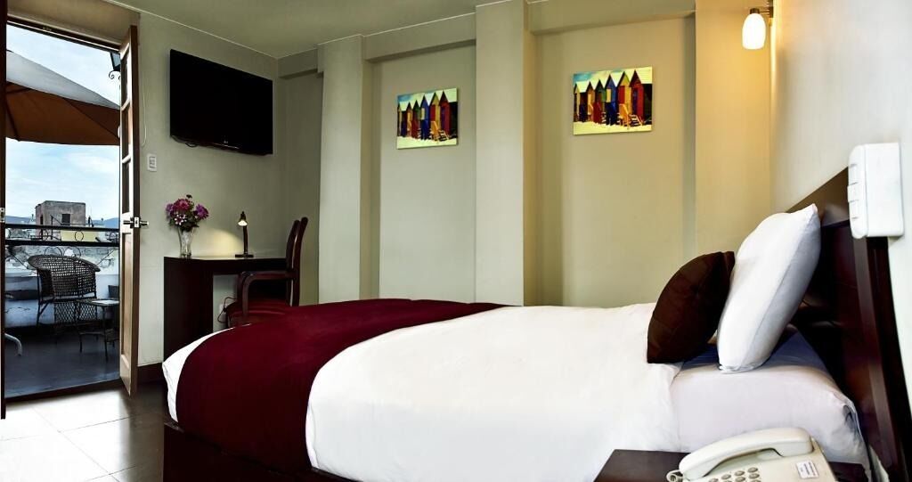 A hotel room with a bed, a desk with a lamp, a phone, and a TV on the wall.