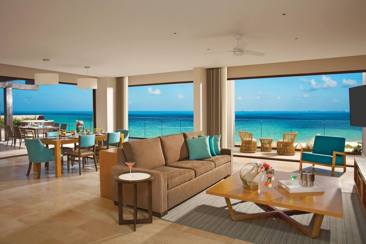 A spacious living room with a large window overlooking the ocean, a sofa, a coffee table, and a dining area with chairs.