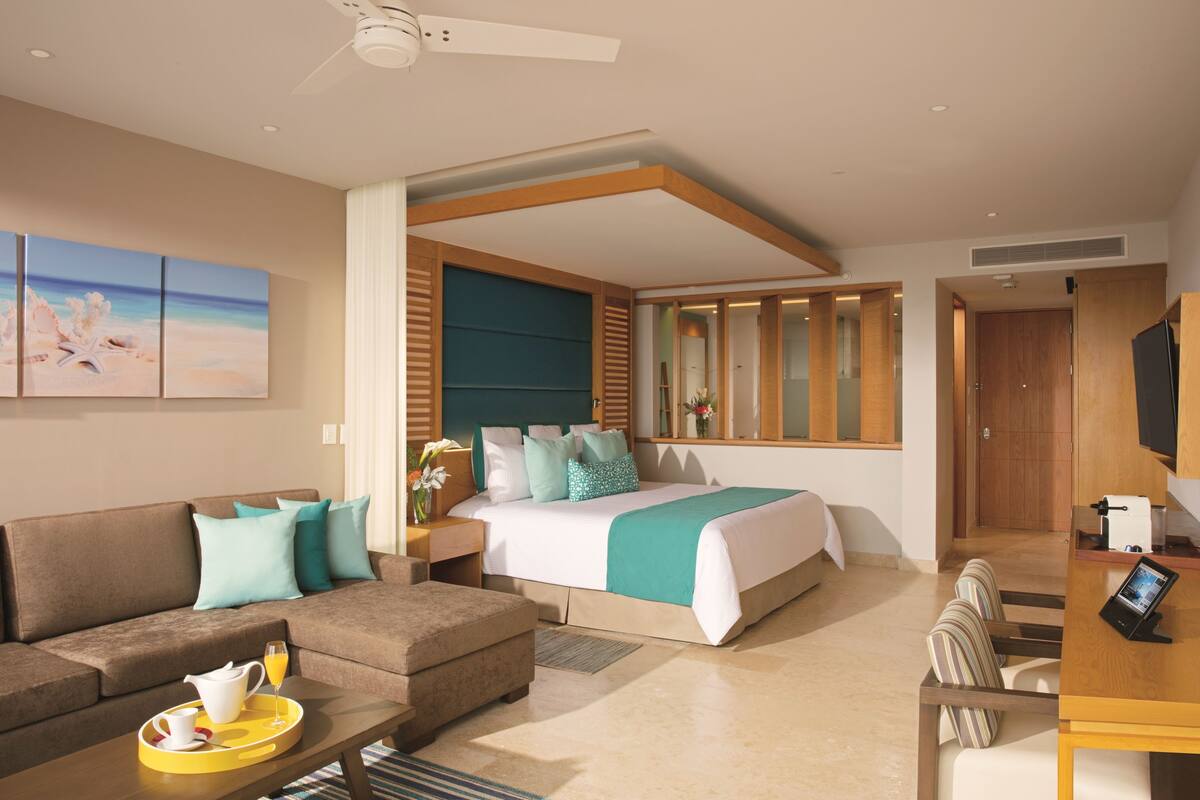 A modern hotel room with a large bed, a sofa, a dining table, and a TV.