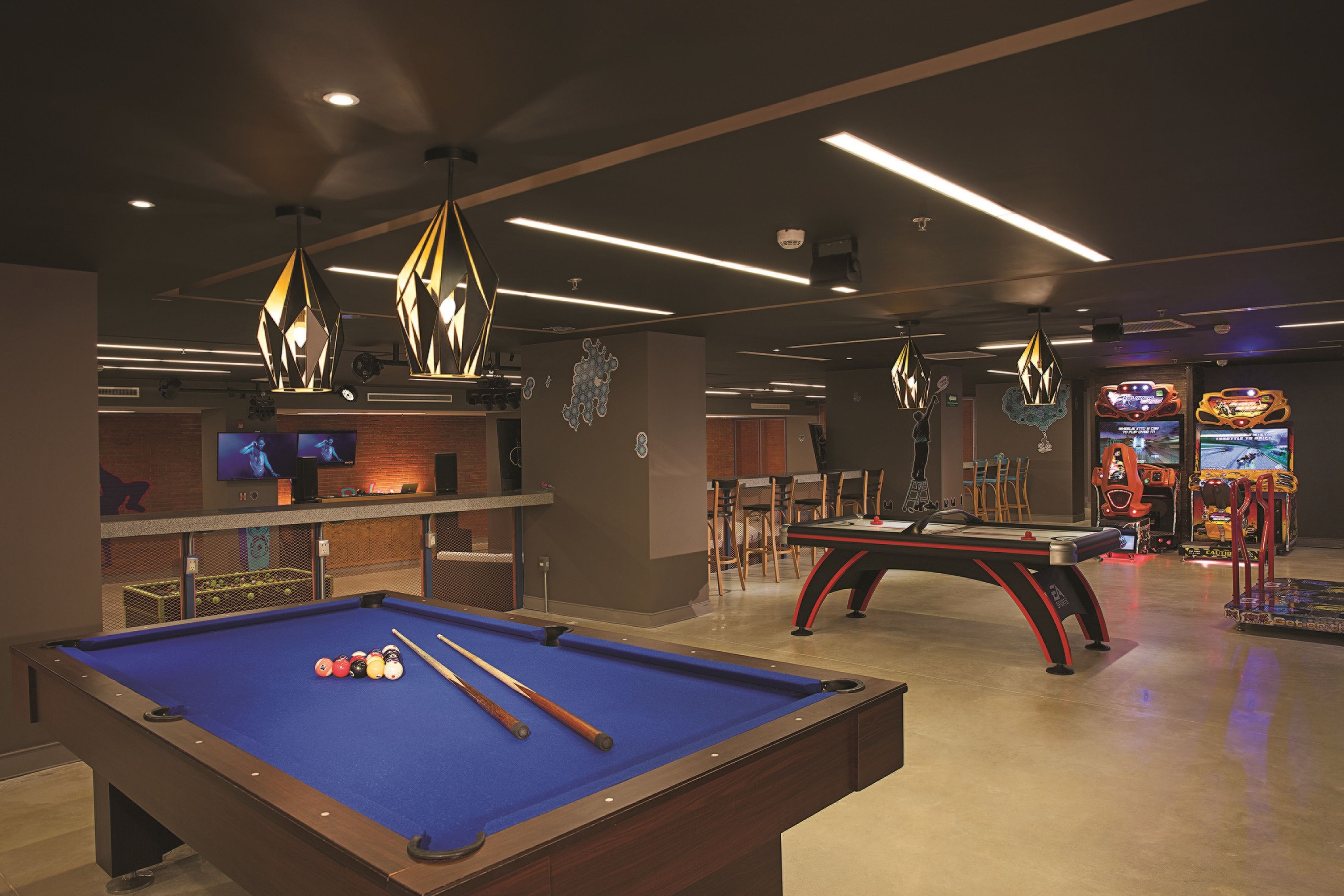 A pool table with billiard balls, a bar area with a TV, and arcade games in a dimly lit room.