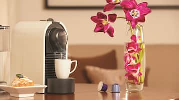 Une machine à café, une tasse, une assiette avec une pâtisserie et un vase rempli de fleurs, le tout posé sur une table.