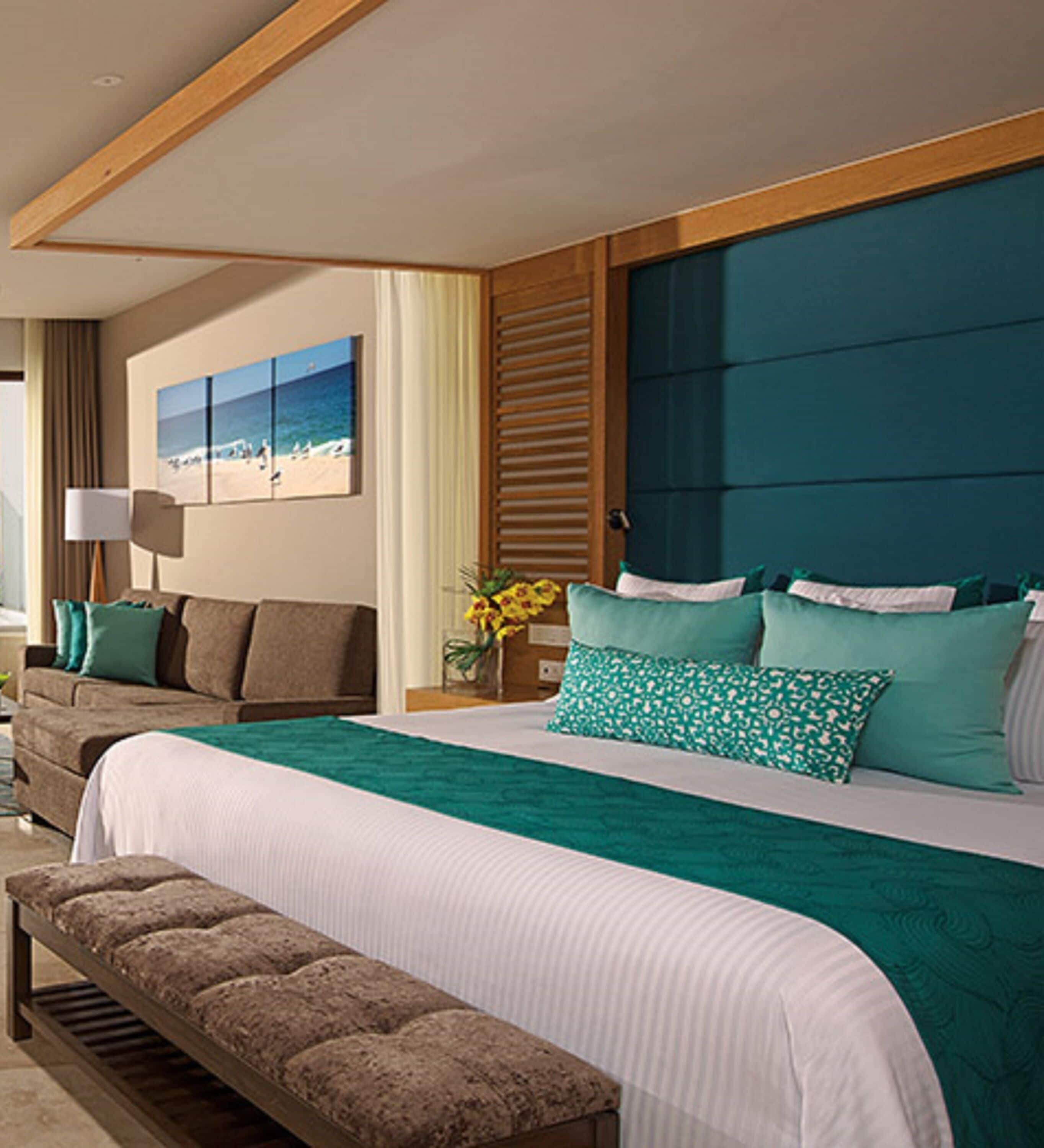 A hotel room with a large bed, a bench, a sofa, and a painting of a beach scene.