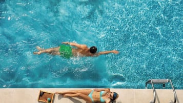 A swimming pool with a person swimming and another person sunbathing on the edge.