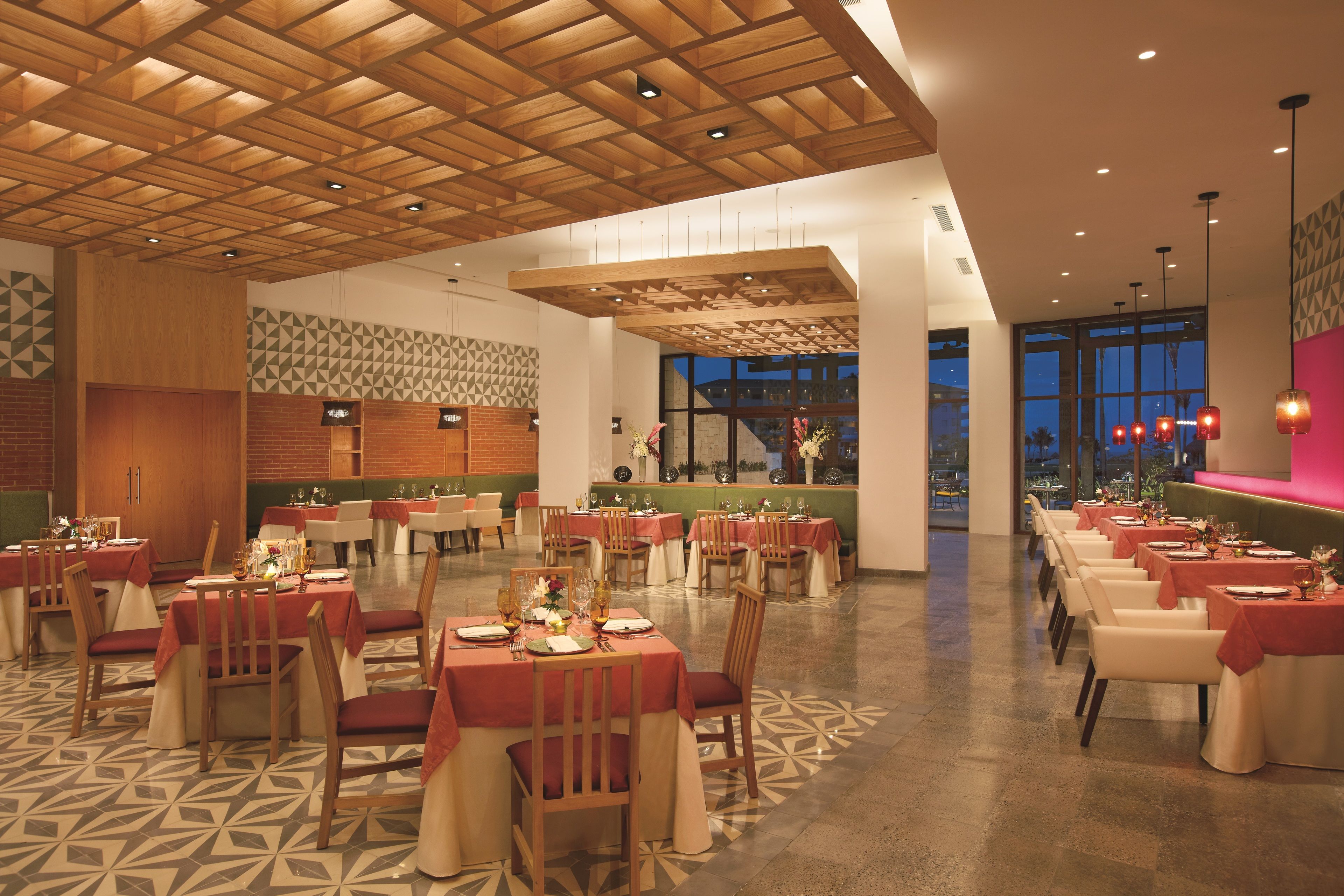 A spacious restaurant with multiple dining tables, wooden ceiling beams, and a patterned floor.