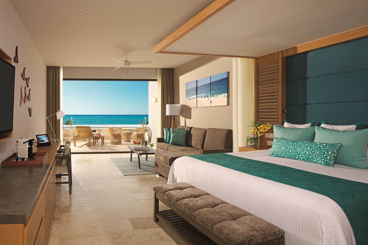 A hotel room with a large bed, a seating area with a view of the ocean, a desk with a computer, and a television on the wall.
