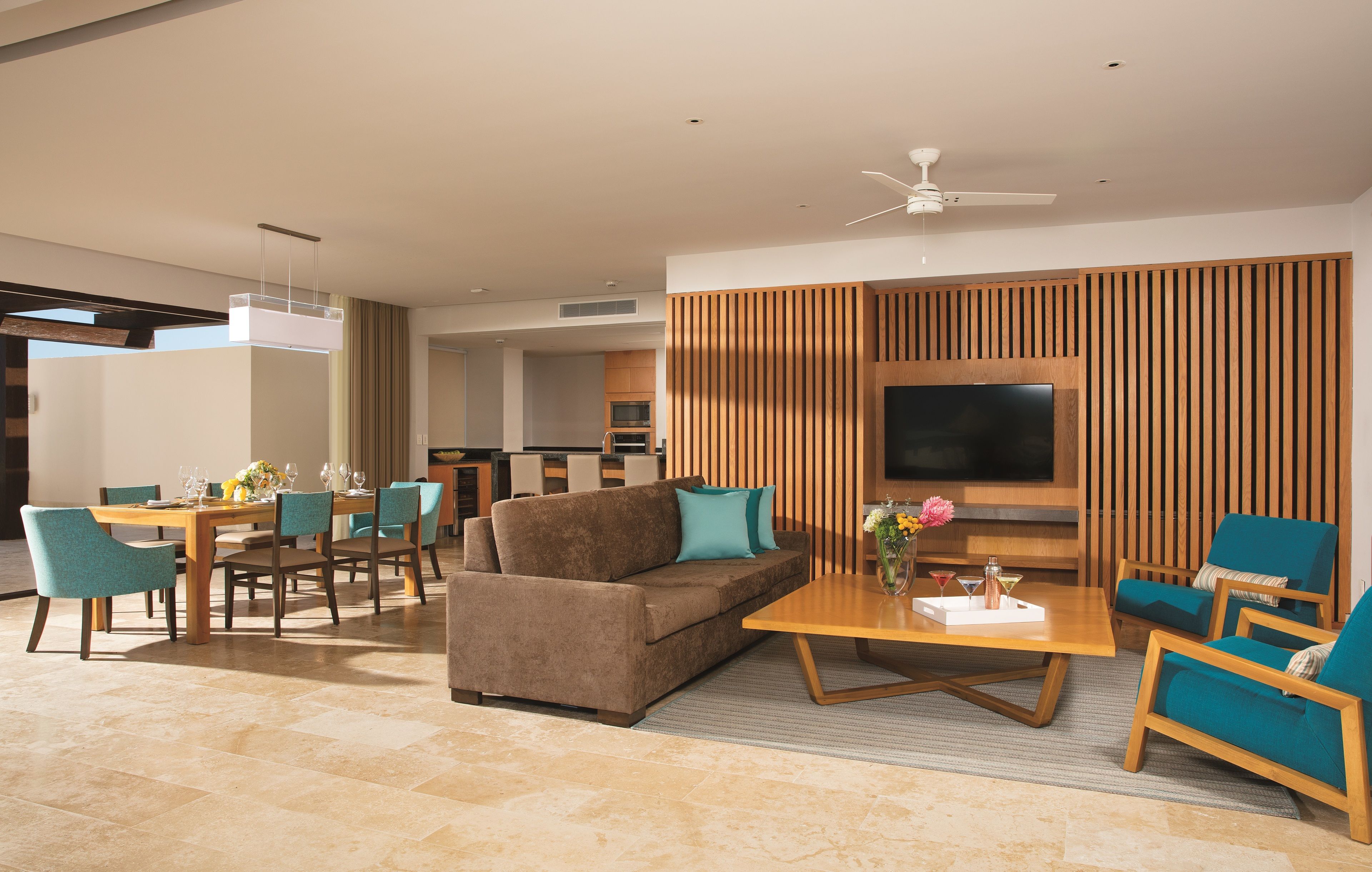 A modern living room with a sofa, coffee table, and chairs, a dining area with a table and chairs, and a kitchen in the background.