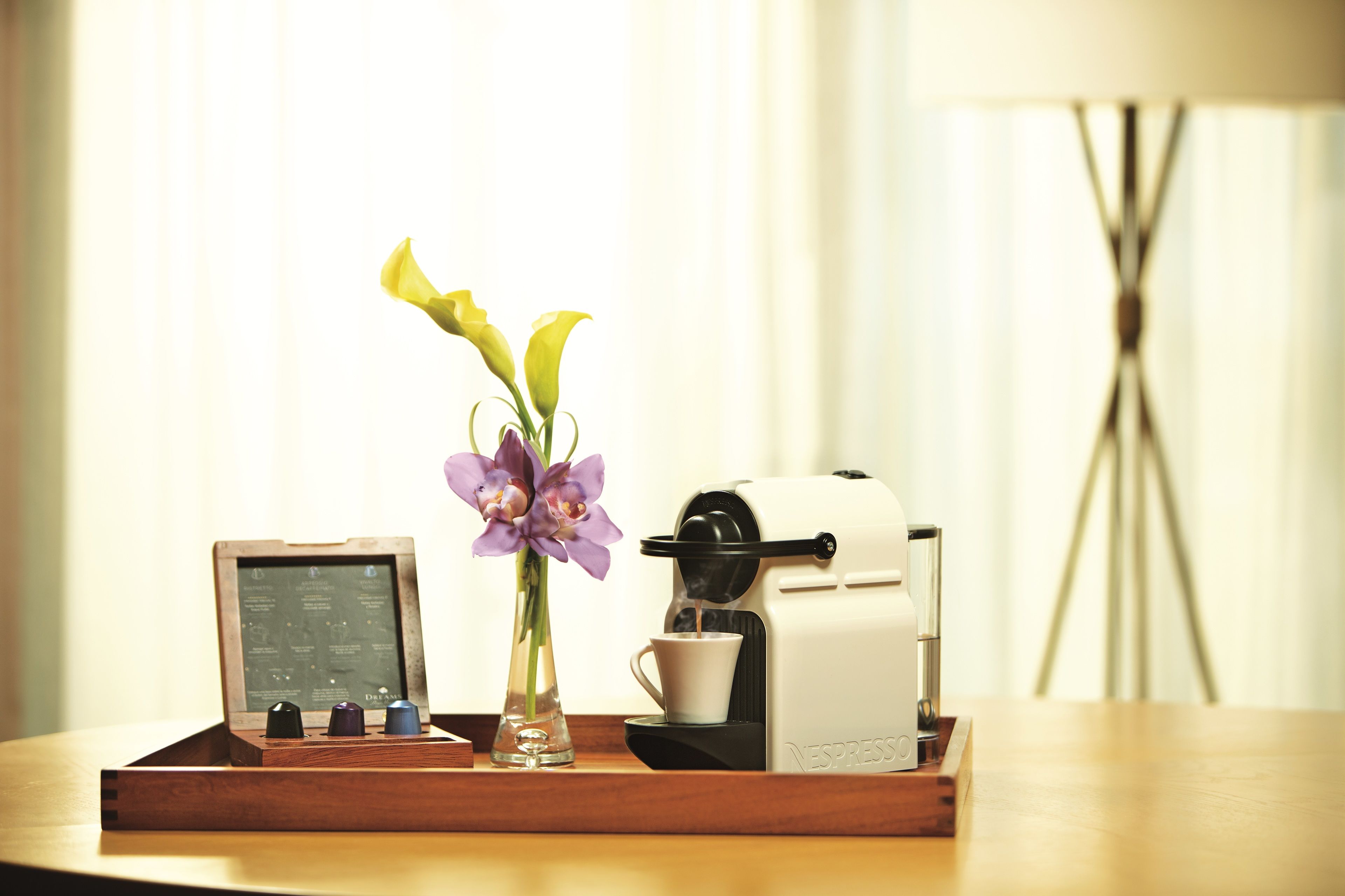 Une machine à café sur un plateau, accompagnée d’un menu, d’un vase avec des fleurs et d’une lampe en arrière-plan.