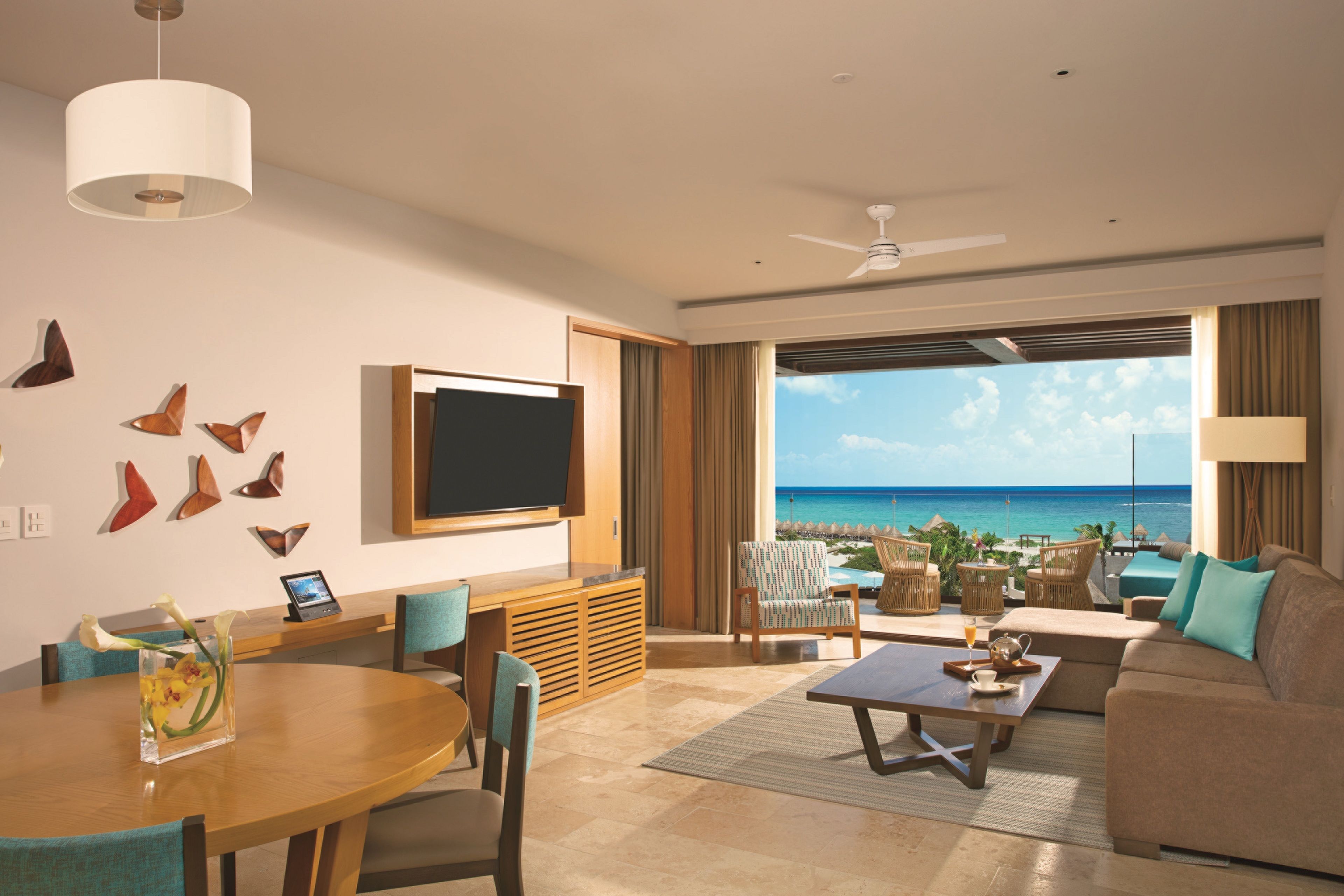 A modern hotel room with a large TV, comfortable seating, a dining area, and a view of the ocean.