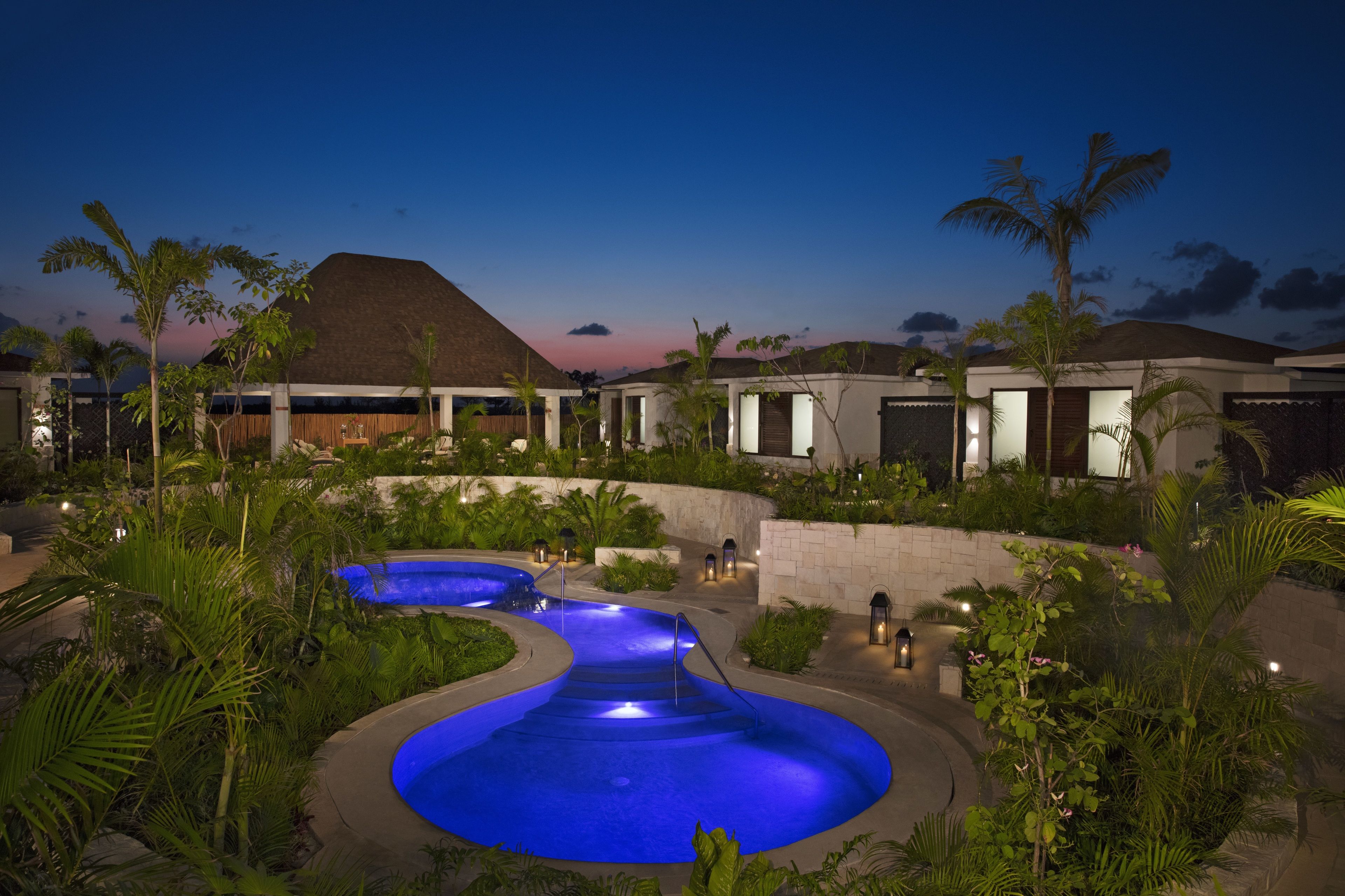 A resort with a swimming pool, palm trees, and a sunset in the background.