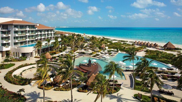 Un resort con una piscina grande, palmeras y vista al mar.