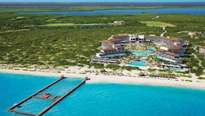 Eine Vogelperspektive eines Resorts mit mehreren Gebäuden, einem großen Schwimmbecken und einem Steg, der ins Meer führt.