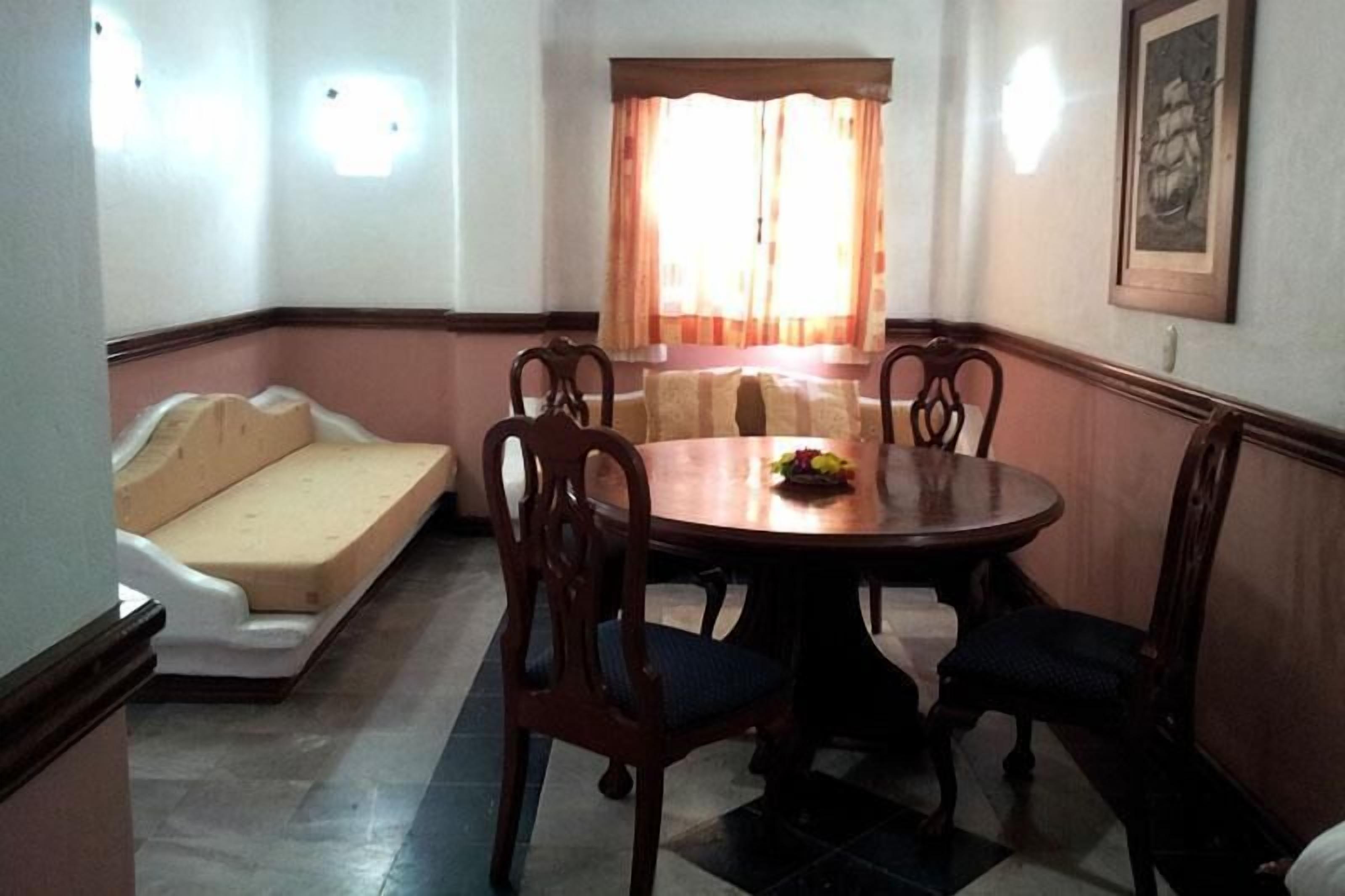 A dining area with a round table, four chairs, a sofa, and a window with curtains.