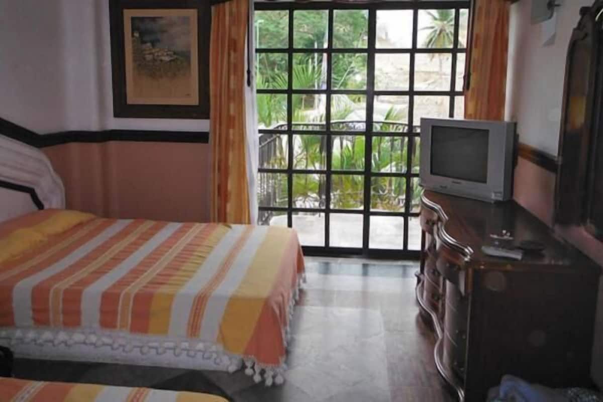 Een hotelkamer met een bed, een televisie op een houten dressoir en een groot raam met uitzicht op groen.