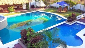 A swimming pool with a thatched roof structure, surrounded by lounge chairs and umbrellas. - Canadian Resorts Huatulco (Santa María Huatulco)