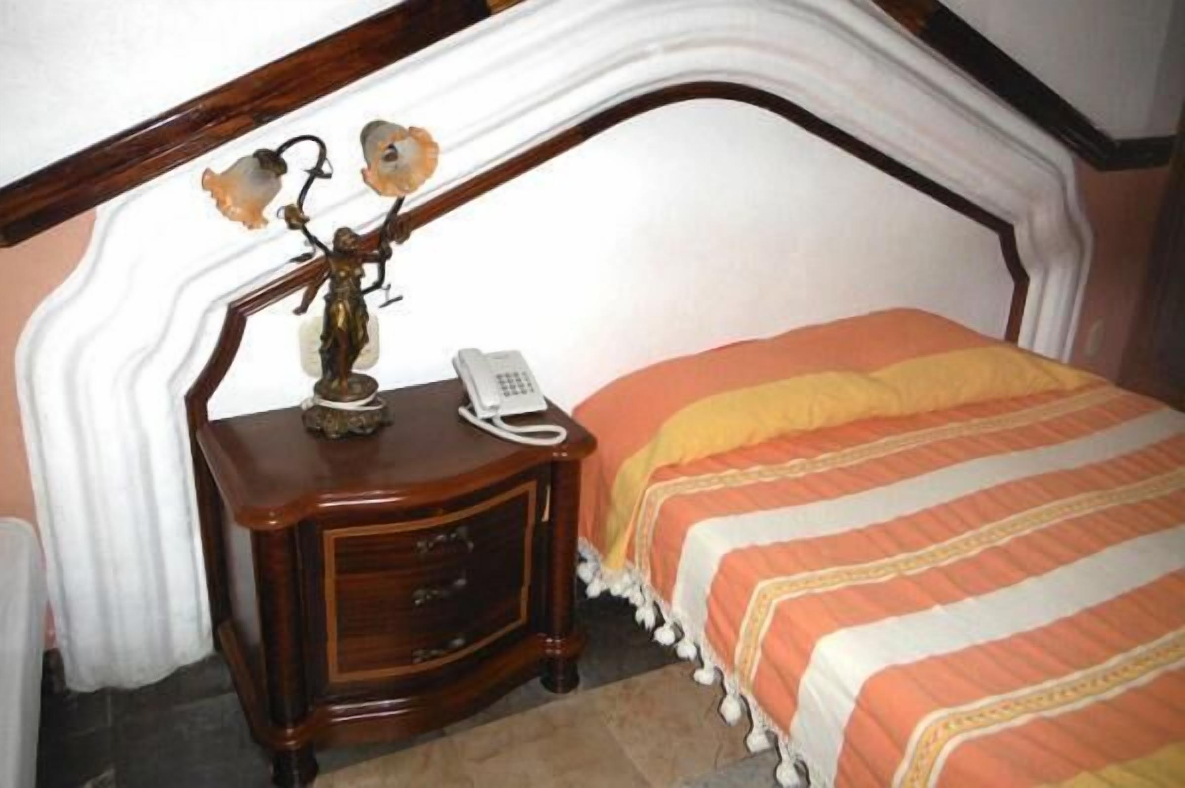 A bedroom with a bed, a nightstand, a telephone, and a decorative lamp.