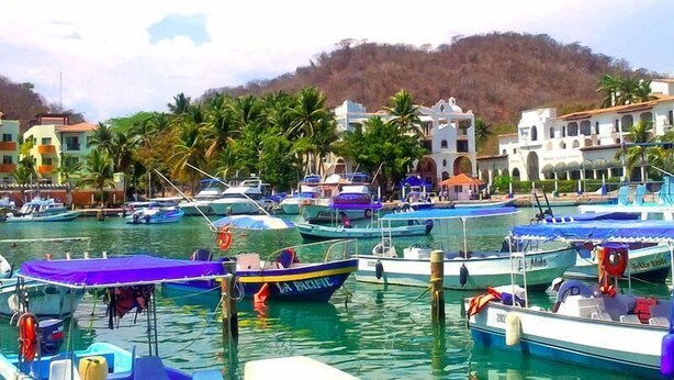 A marina with multiple boats docked, surrounded by buildings and palm trees. - Canadian Resorts Huatulco (Santa María Huatulco)