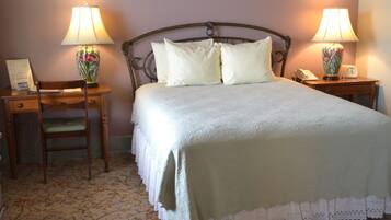 A neatly made bed with a green bedspread and white pillows, flanked by two nightstands with lamps and a chair.