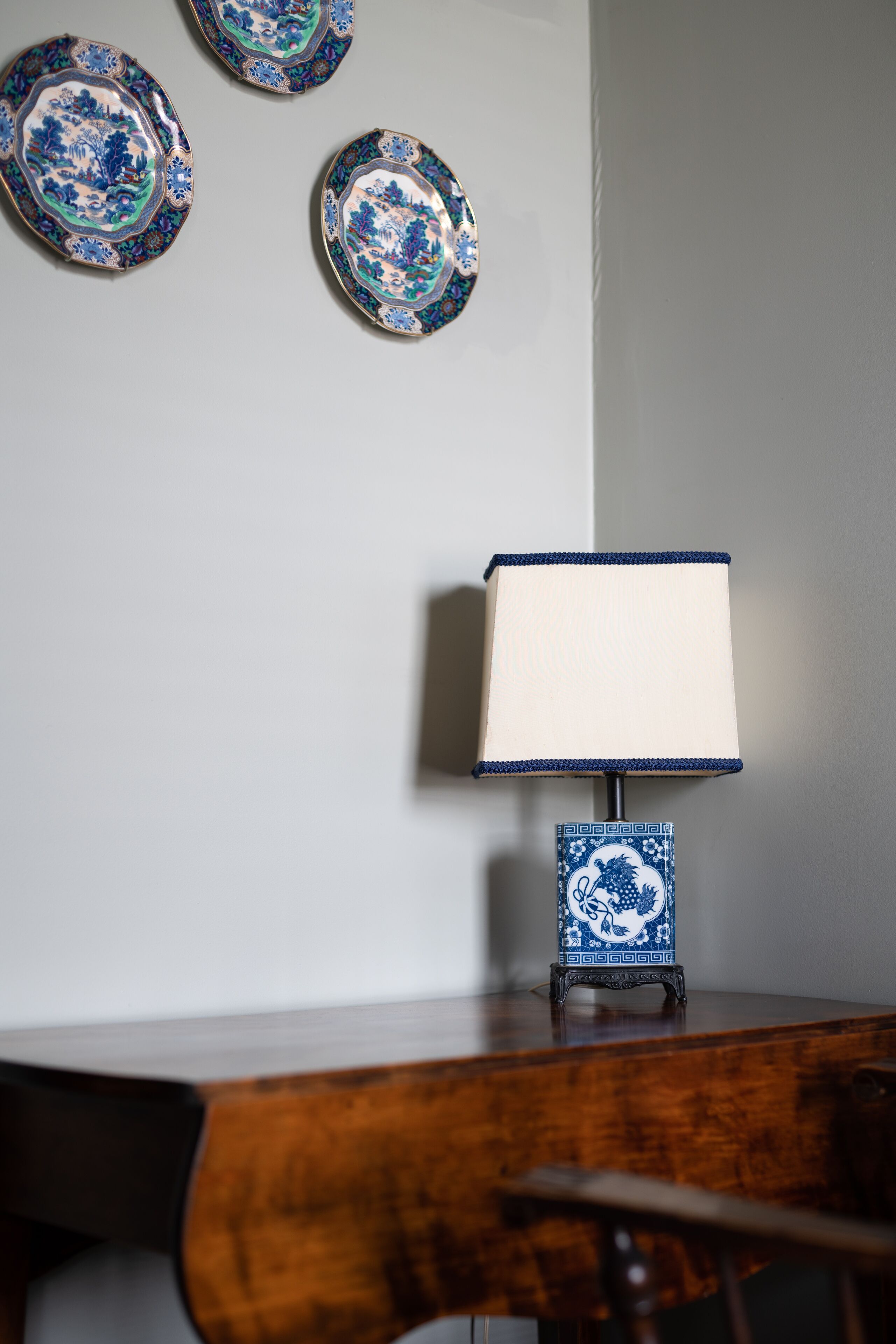 A wooden desk with a blue and white patterned lamp and three decorative plates on the wall.