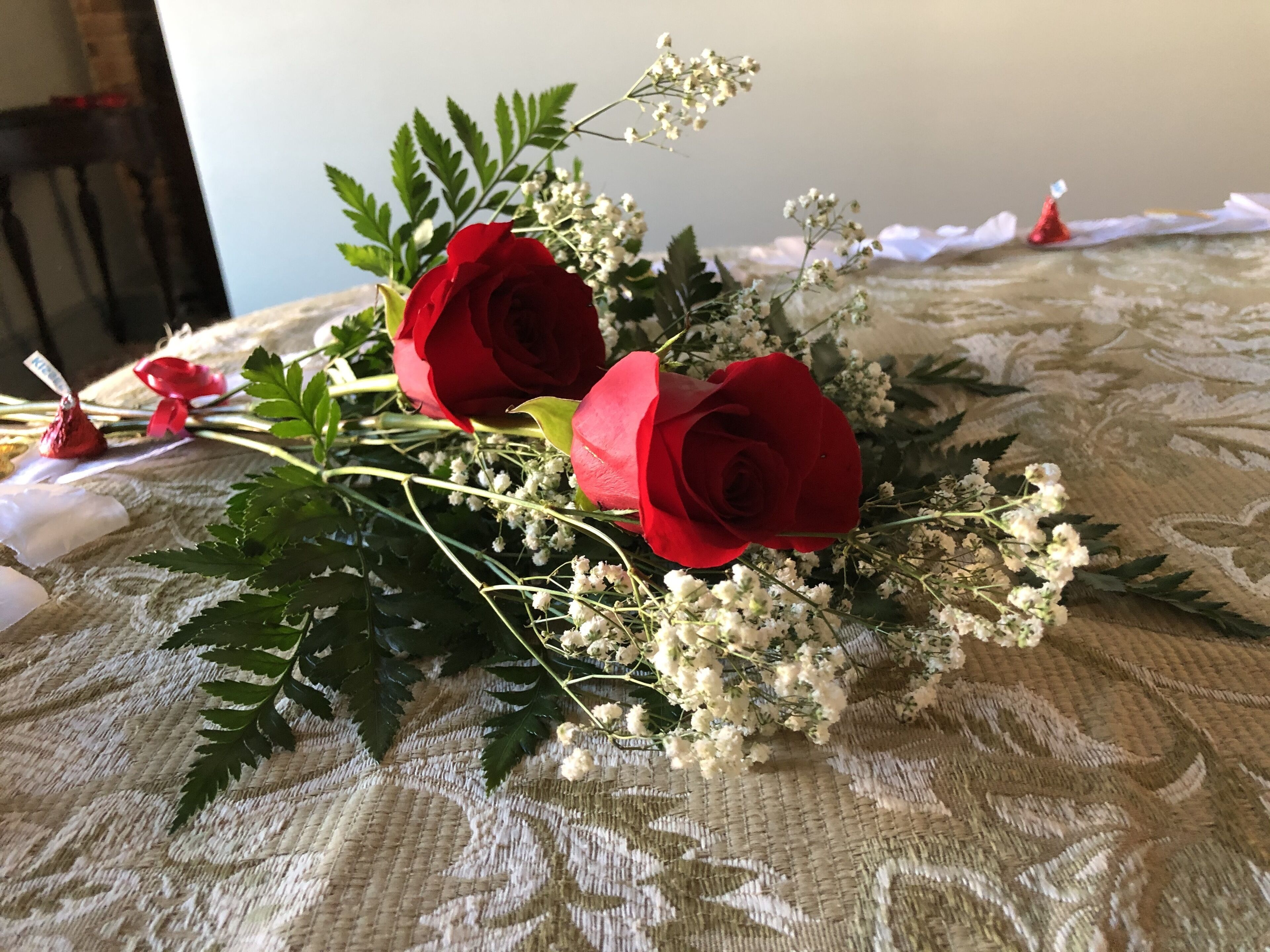 A bouquet of red roses and baby's breath on a patterned tablecloth.