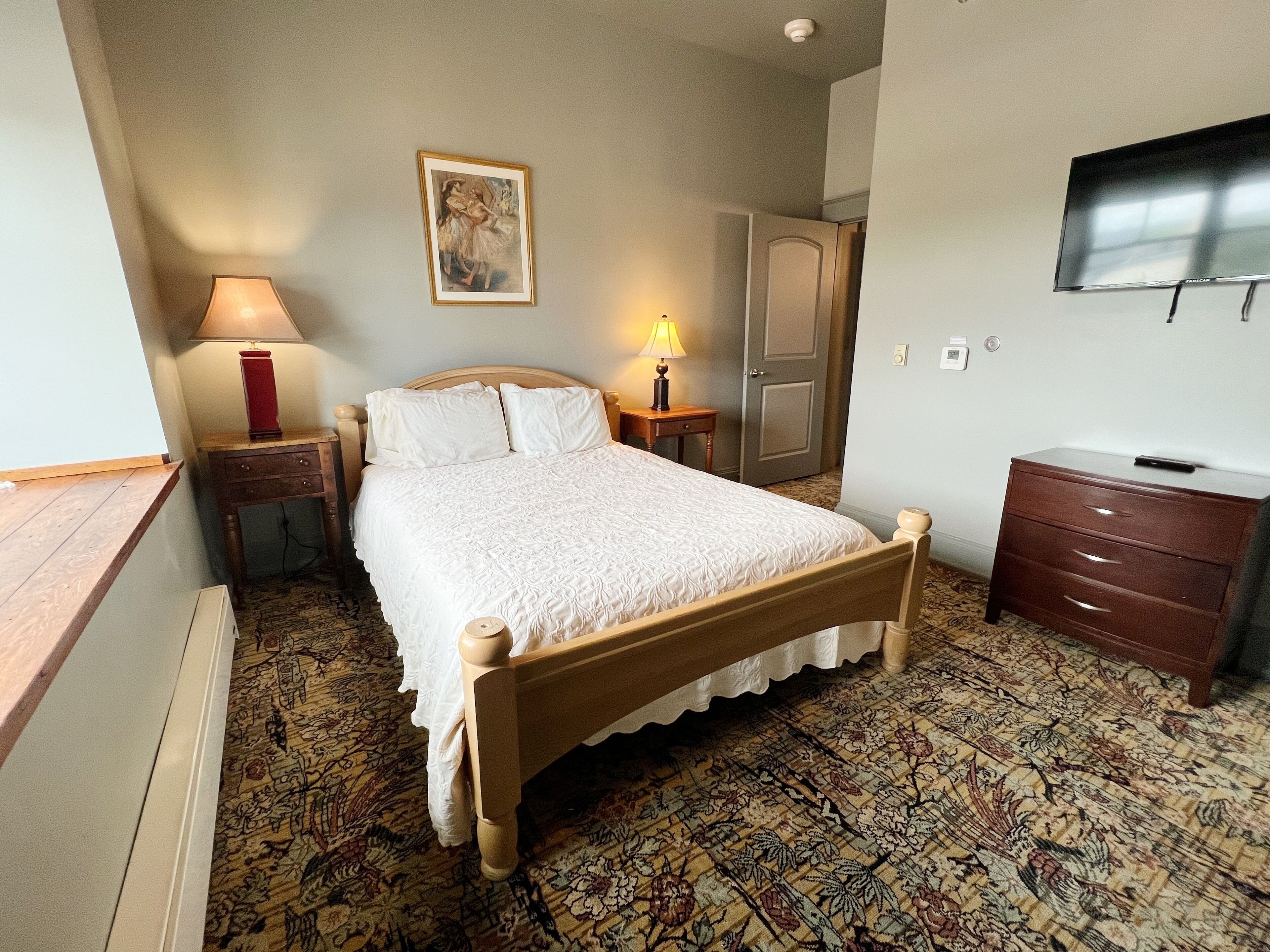 Una camera da letto ordinata con un letto di legno, un comodino con una lampada, una cassettiera, un armadio e una televisione a parete.