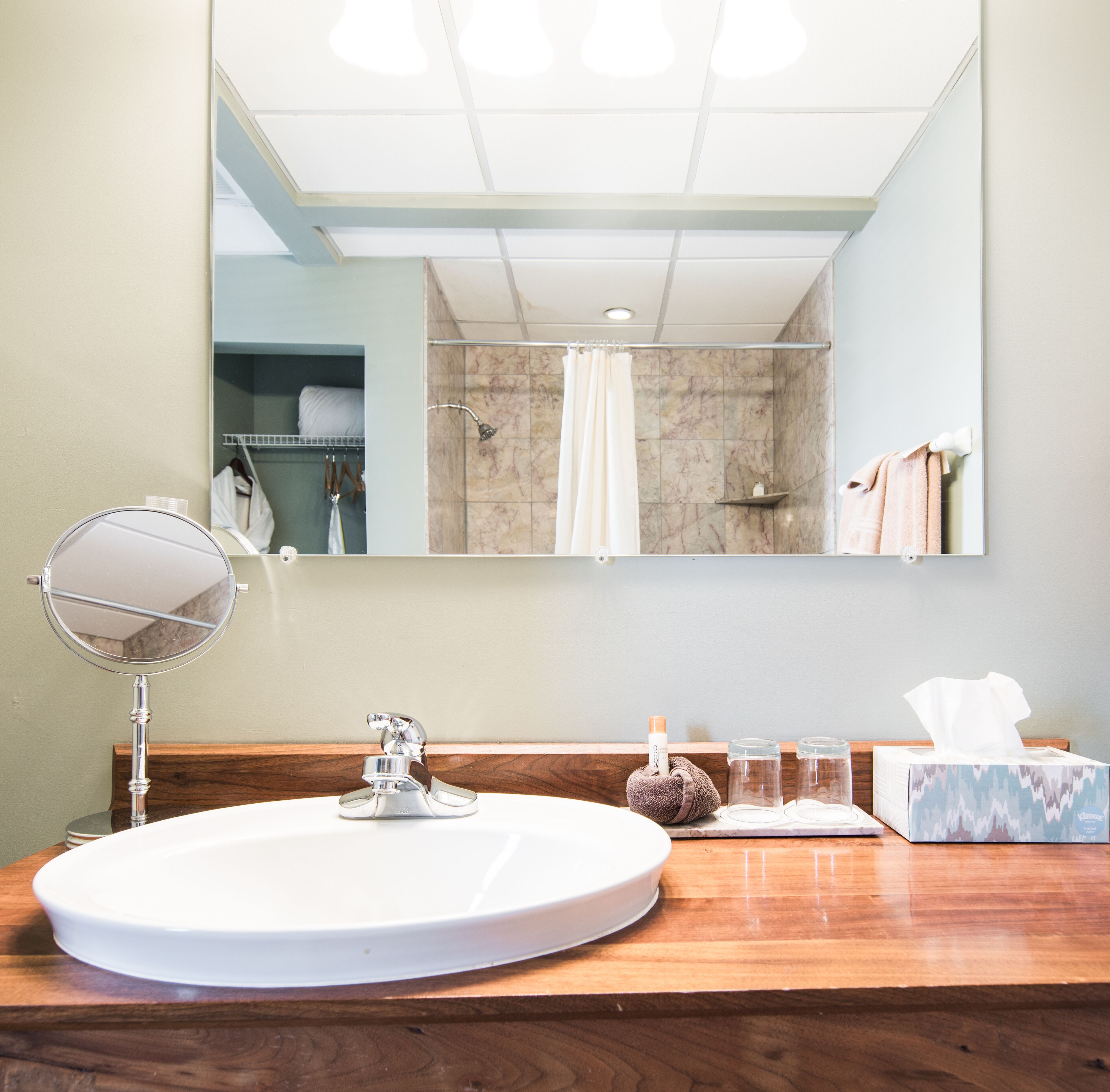 A bathroom with a round sink, a mirror, a towel rack, and a shower area.