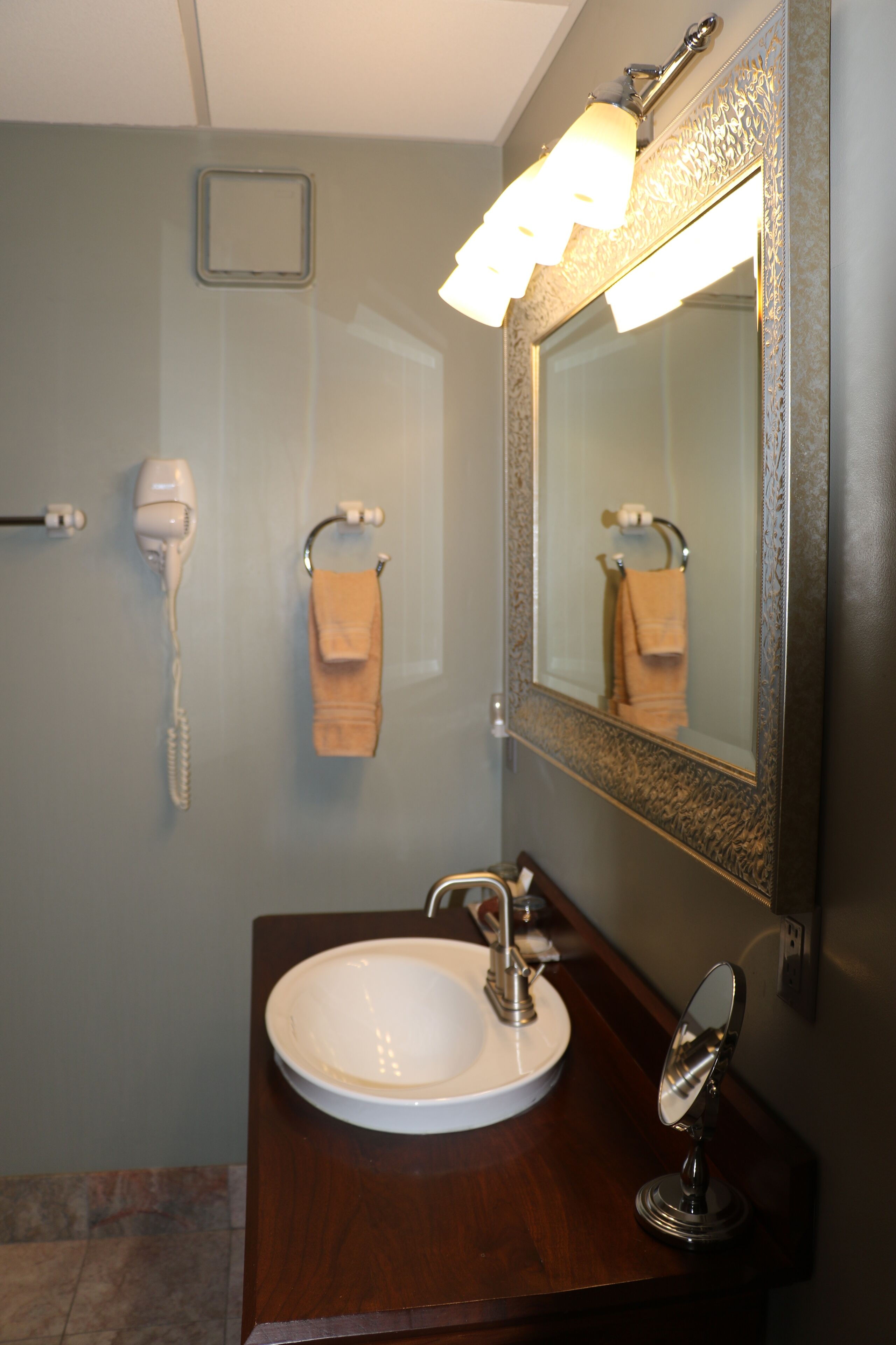 Un baño con lavamanos blanco, espejo, toallero y secador de pelo.