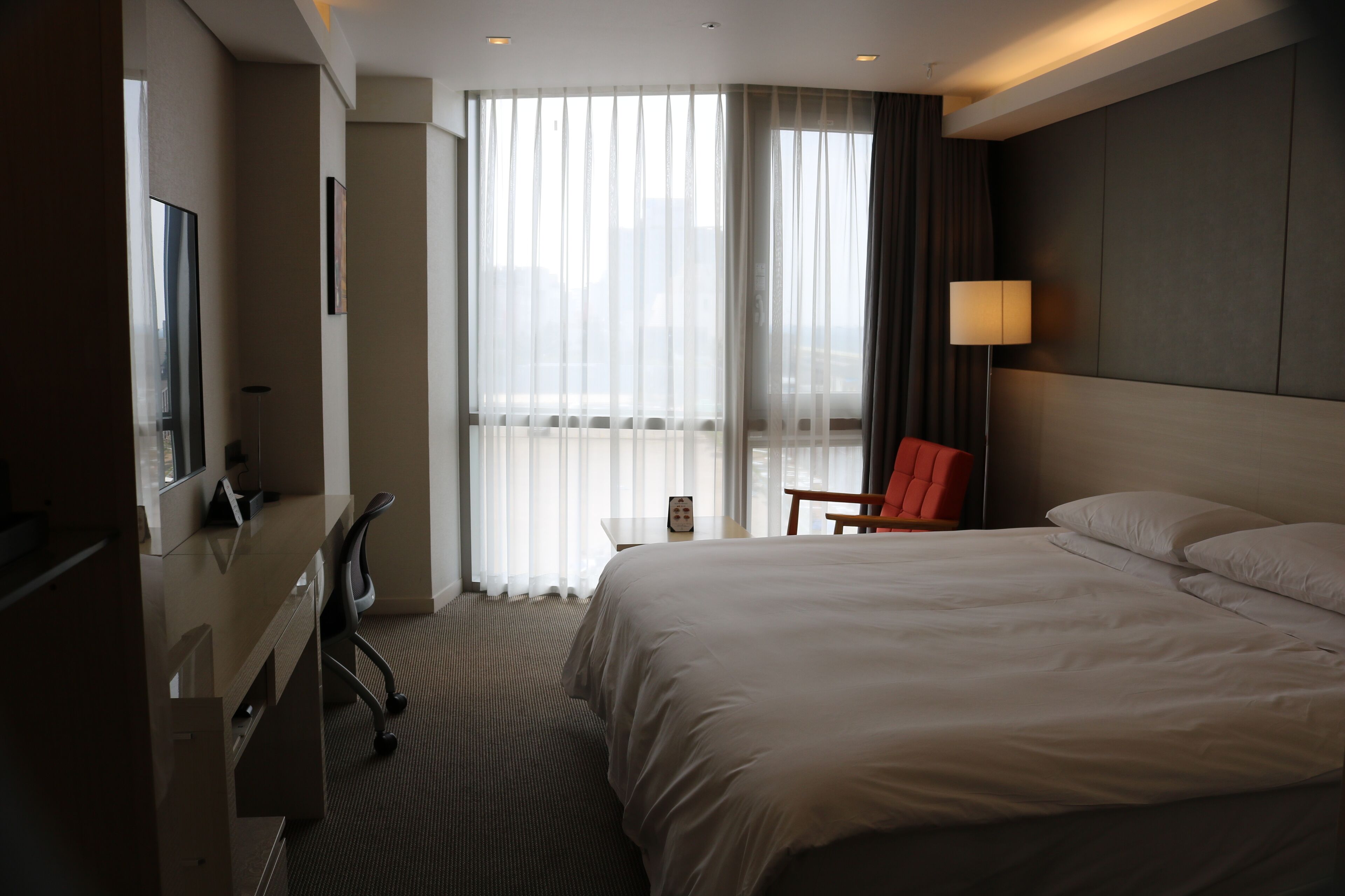 Habitación de hotel con una cama grande, un escritorio con silla, televisión y ventana con cortinas.