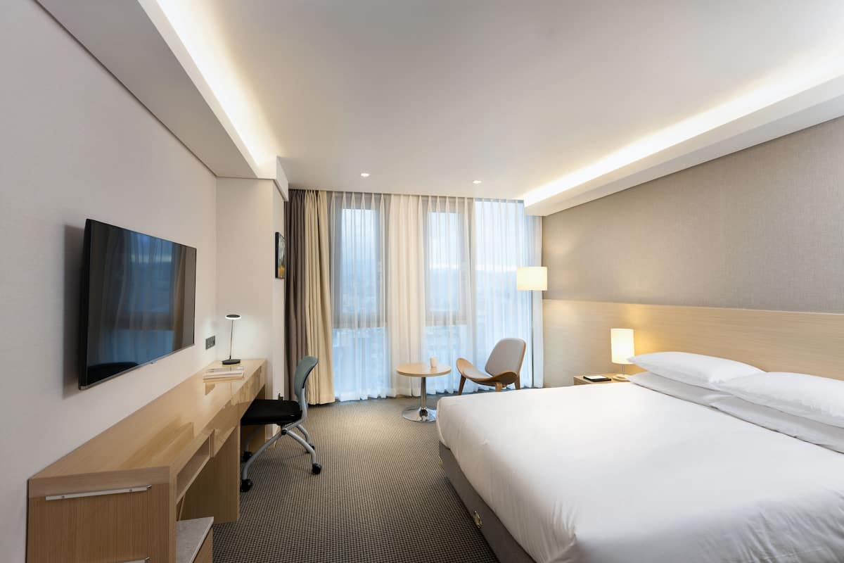 Une chambre d’hôtel équipée d’un lit, d’un bureau, d’une chaise, d’une télévision et d’une fenêtre avec des rideaux.
