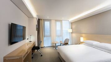 A hotel room with a bed, desk, chair, TV, and a window with curtains.