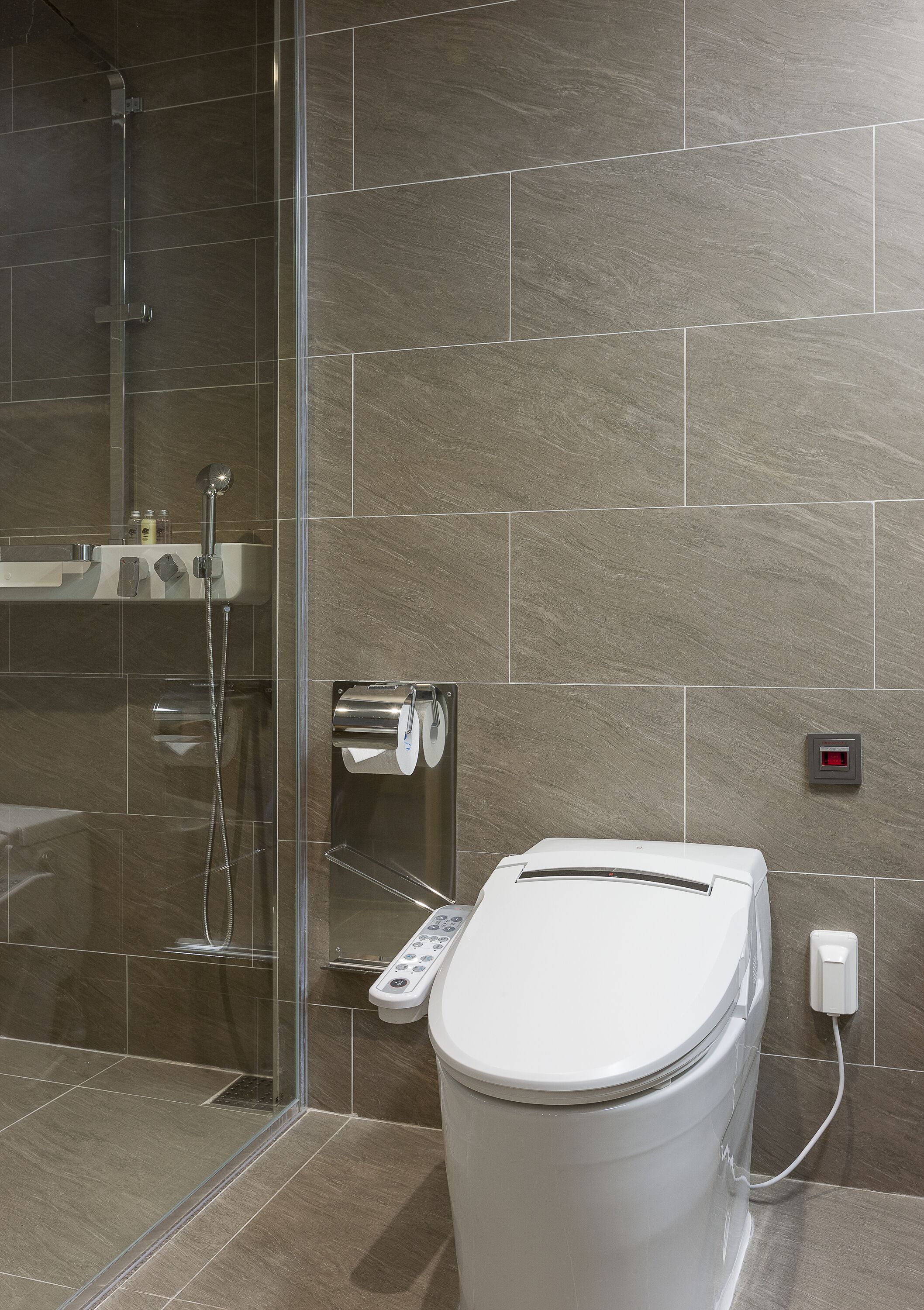 Une salle de bain moderne avec une douche à parois de verre, des toilettes dotées d’un panneau de commande et un porte-serviettes.