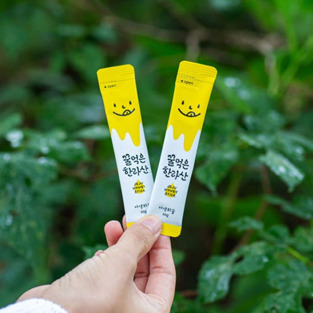 A hand holding two honey sticks with Korean text and a smiling face design.
