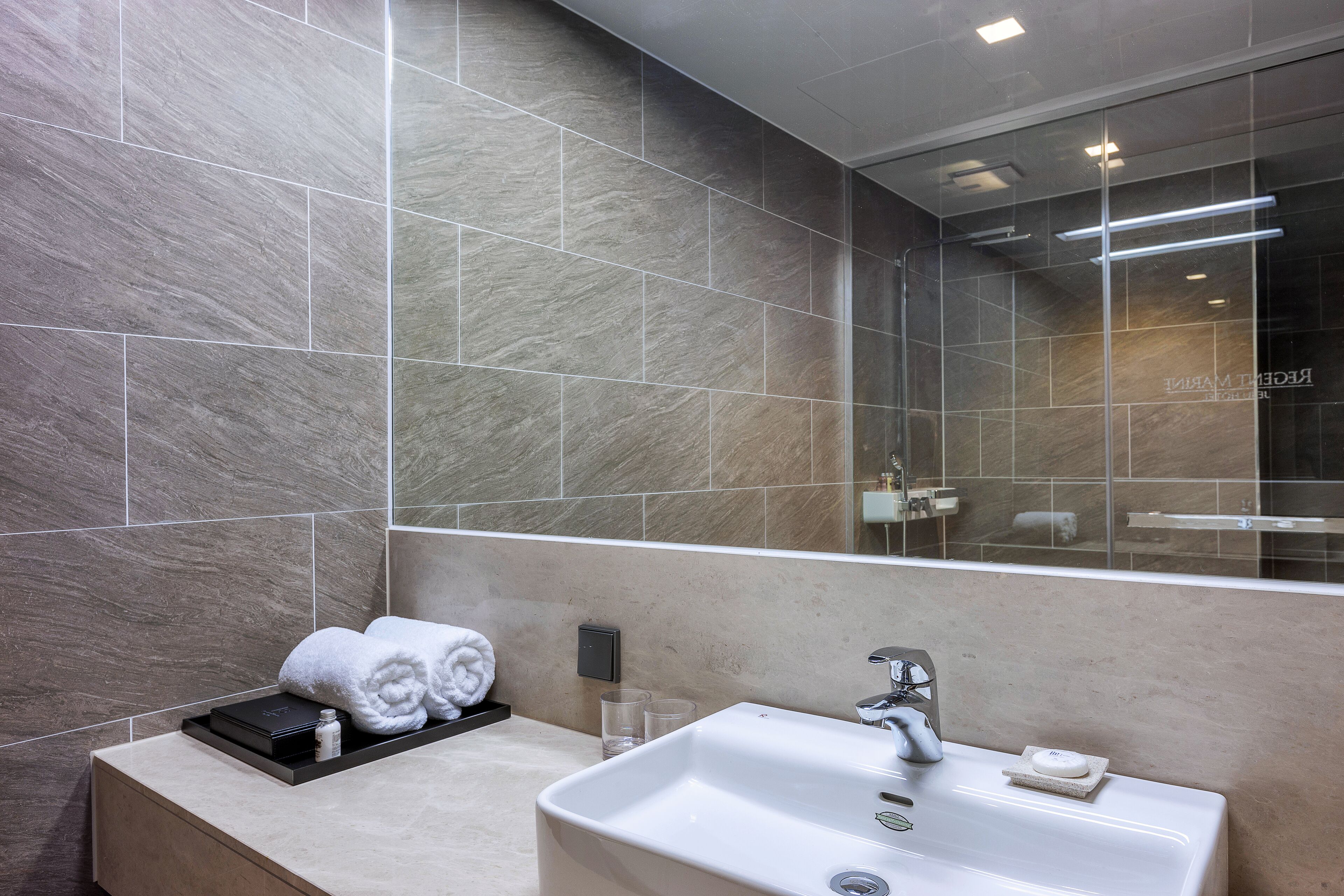 Un bagno moderno con un grande specchio, un lavandino bianco e asciugamani piegati ordinatamente su un vassoio.