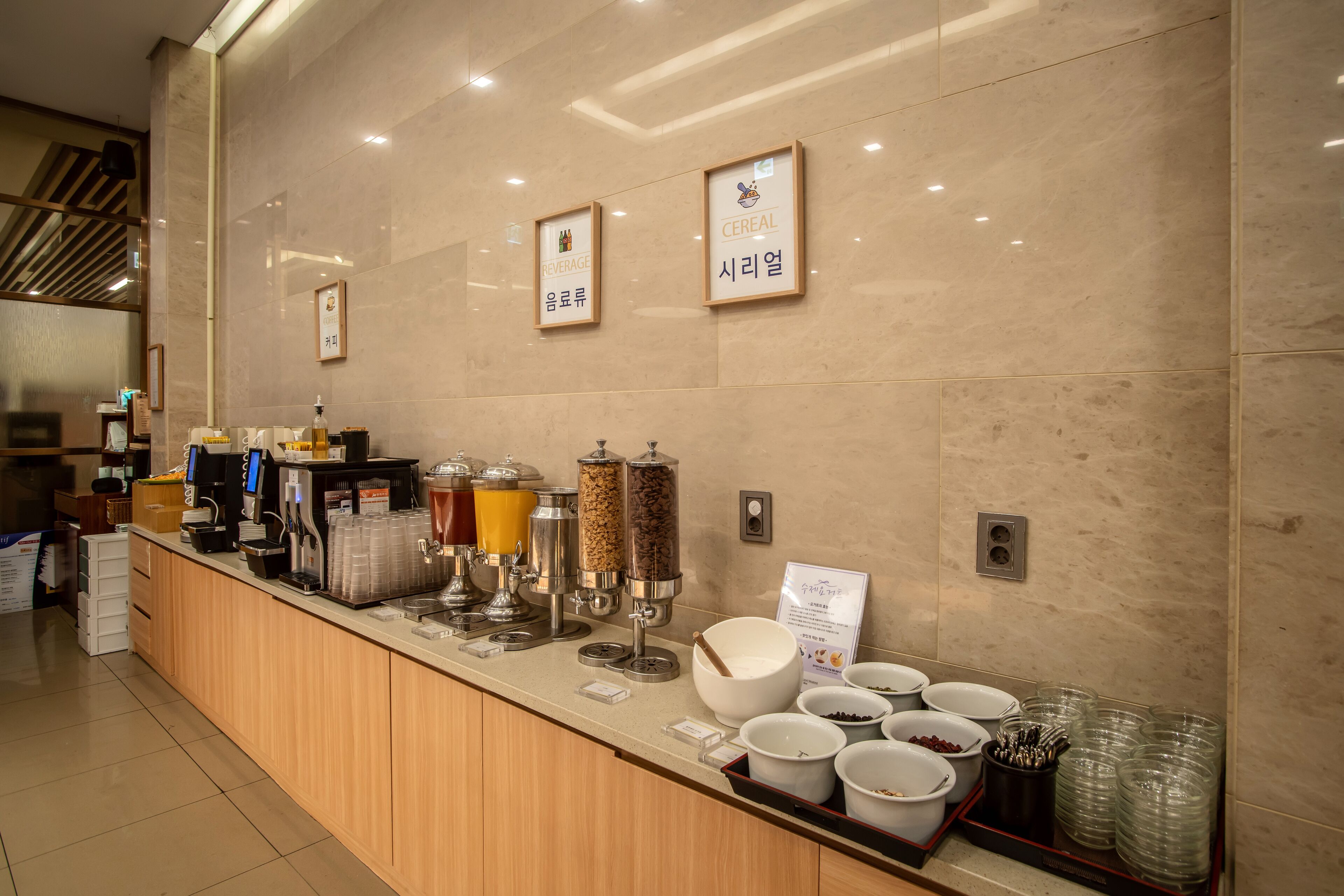 Una barra de desayuno con diferentes dispensadores de alimentos y bebidas, incluyendo una máquina de café, dispensadores de zumo y cereales.