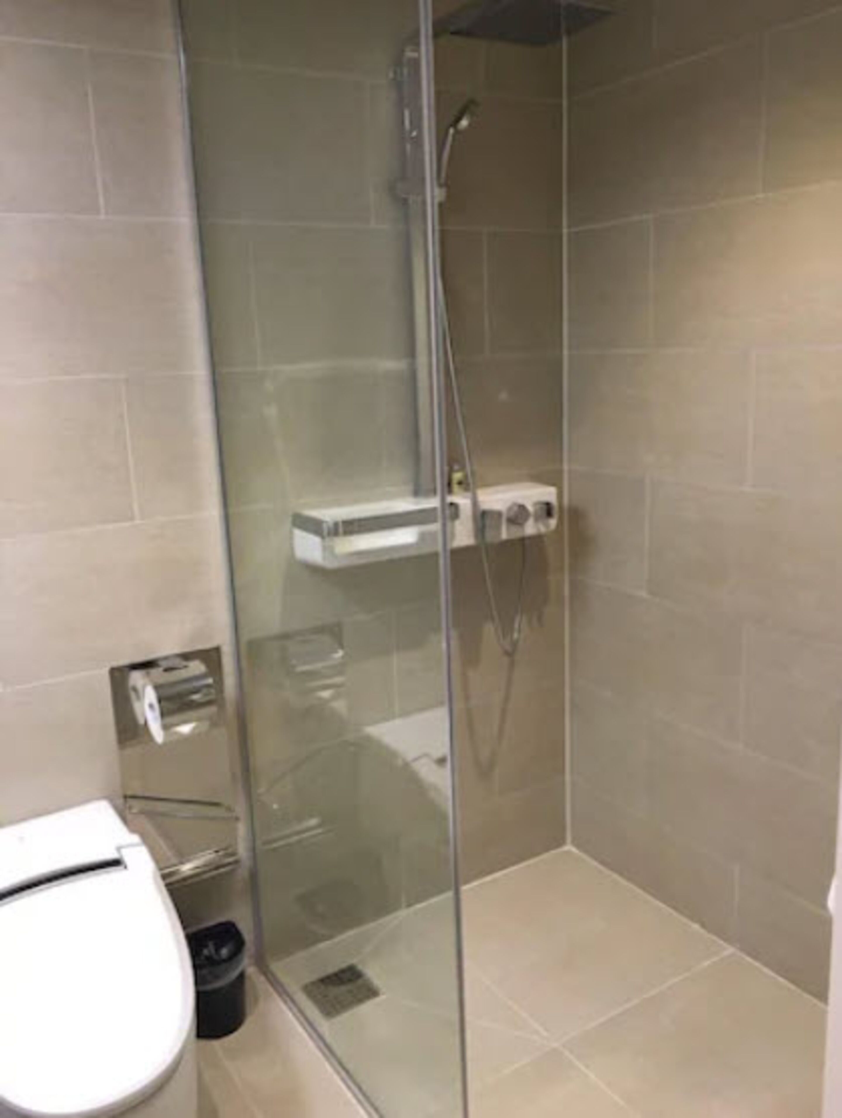 Un baño moderno con ducha acristalada, inodoro y un pequeño armario.