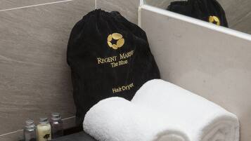 A bathroom vanity with a black hair dryer, a black bag with gold lettering, and two white towels.