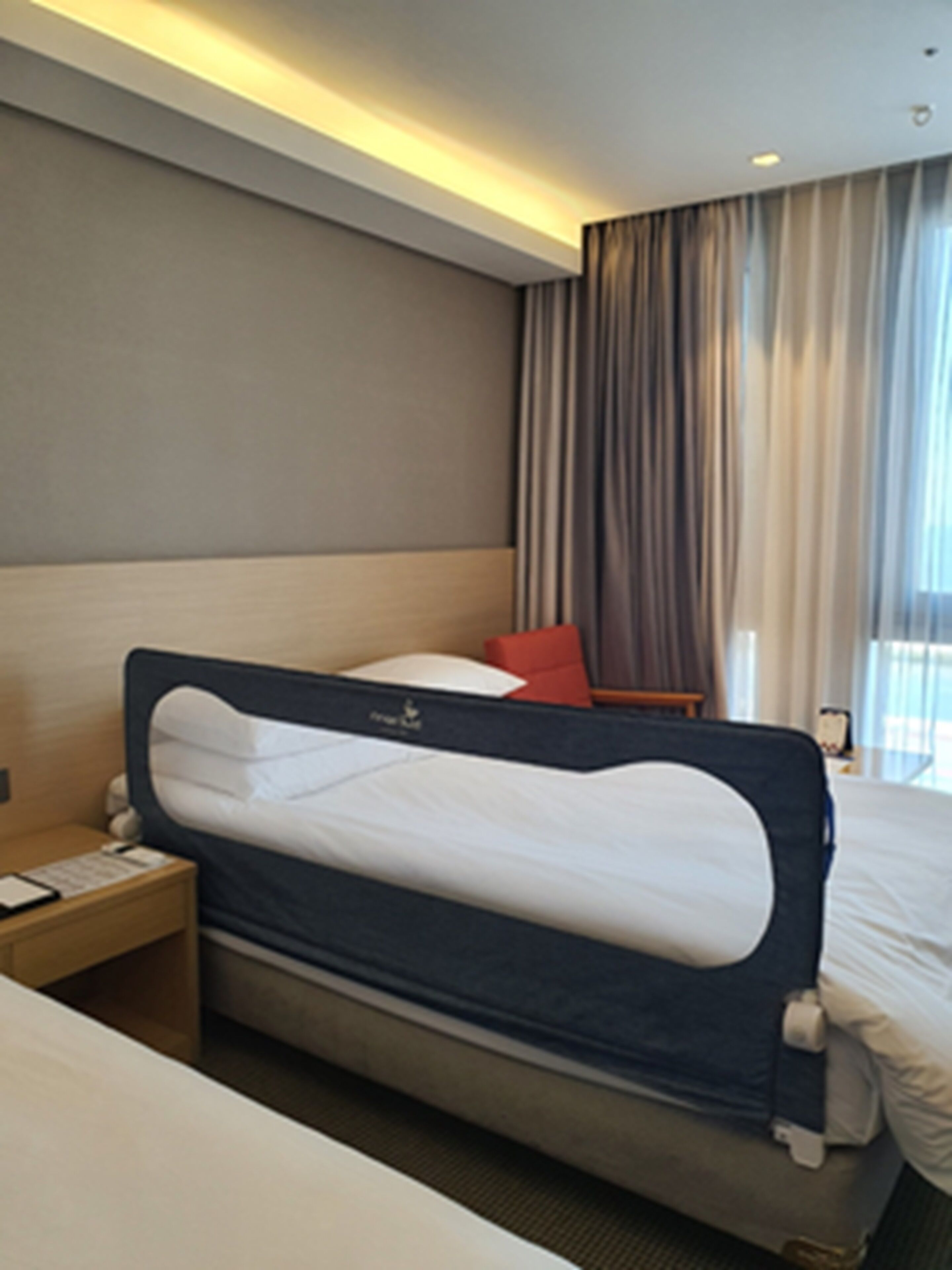 Een moderne hotelkamer met een groot bed, een nachtkastje en een raam met gordijnen.