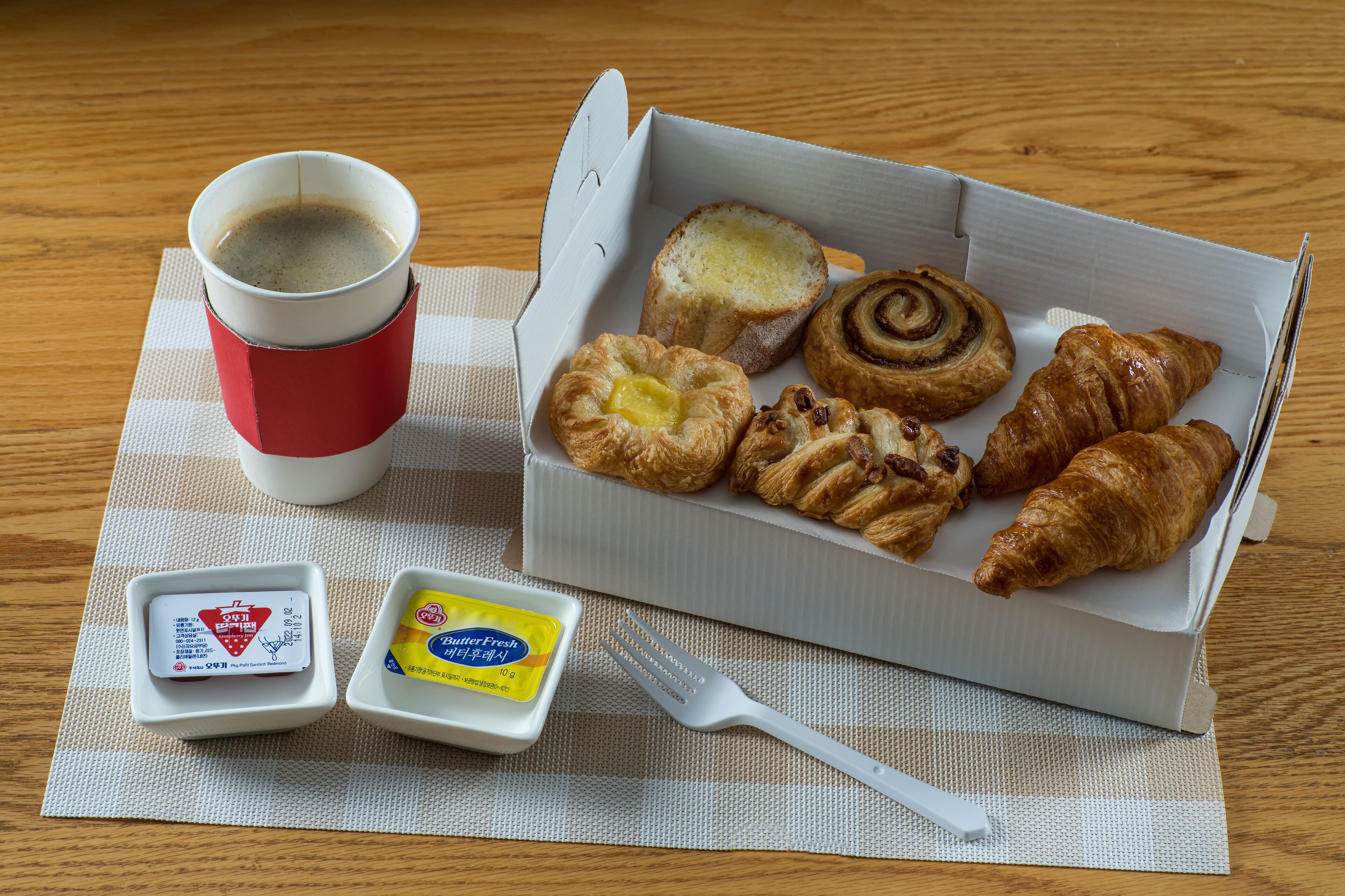 Une table mise pour le petit-déjeuner, avec une tasse de café, des croissants et des portions de beurre disposées sur un set de table.